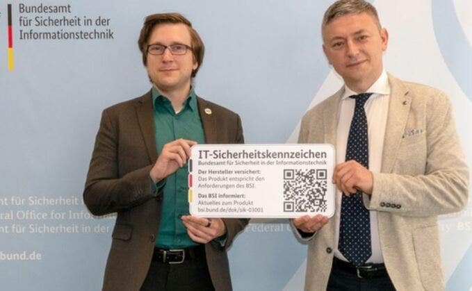 Joshu Wiebe vom BSI (li.) übergibt die zwei IT-Sicherheitskennzeichen an David Baumgart, Xiaomi Technology Germany