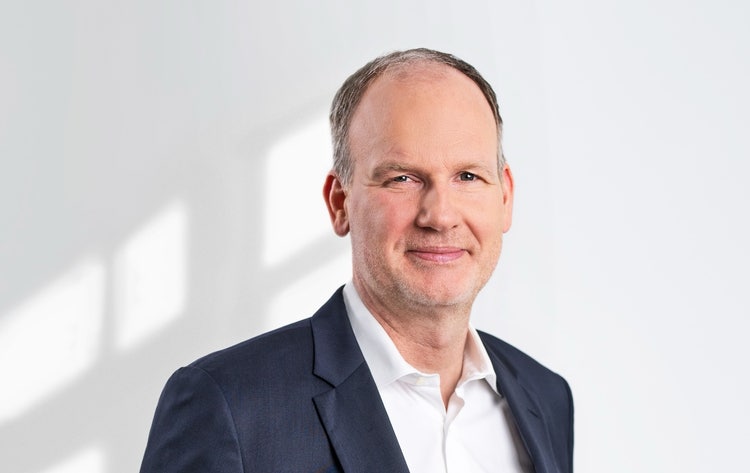 Ein Bild, das Menschliches Gesicht, Person, Kleidung, Unternehmer enthält. Automatisch generierte Beschreibung