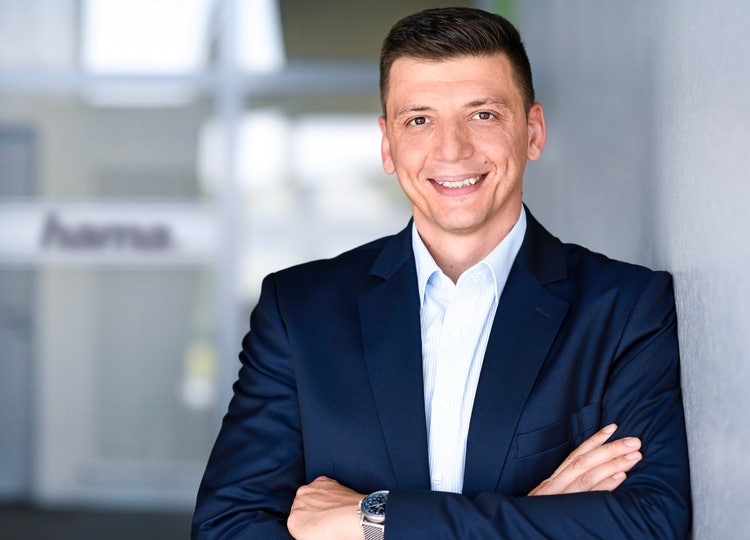 Ein Bild, das Person, Menschliches Gesicht, Lächeln, Formelle Kleidung enthält. Automatisch generierte Beschreibung